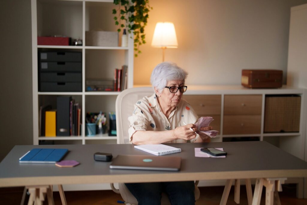 Senior woman counting banknotes while managing personal finances at home office desk